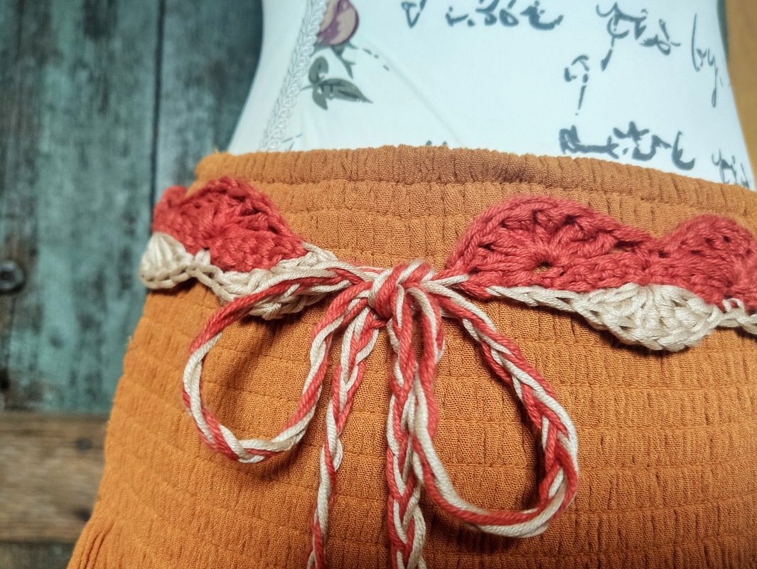 Gehäkelter Taillengürtel mit Blattmotiven und zweifarbiger Kordel an oranger Taille