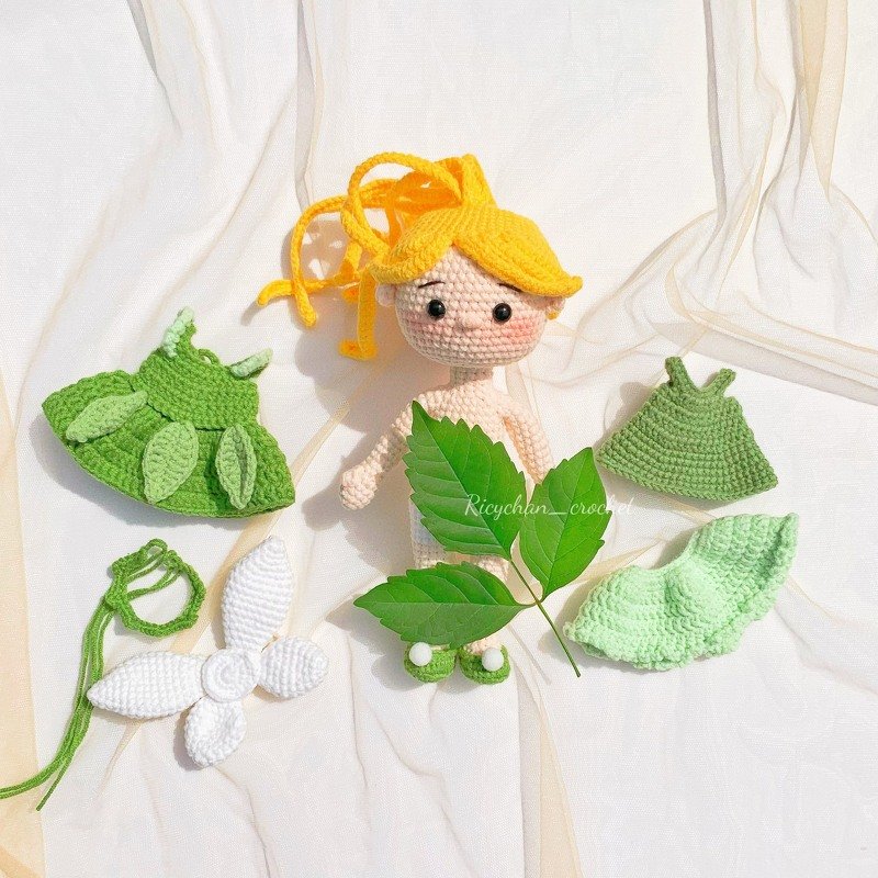 Crocheted amigurumi fairy doll with yellow yarn hair, green dresses, a leaf-style hat, and white wings.