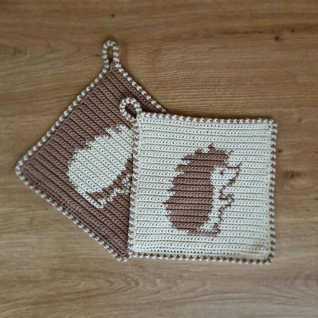 Zwei quadratische gehäkelte Topflappen mit Igelmotiv in Braun und Beige auf Holztisch