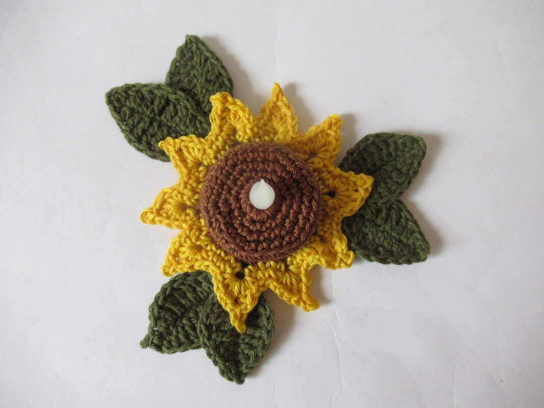 Gehäkelte Sonnenblume mit braunem Kern und drei grünen Blättern