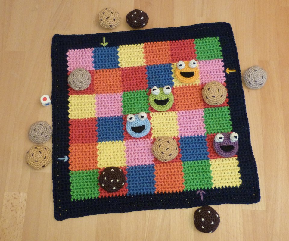 Gehäkeltes Brettspiel mit bunten Farbquadraten, runden Spielsteinen und Gesichtsfiguren