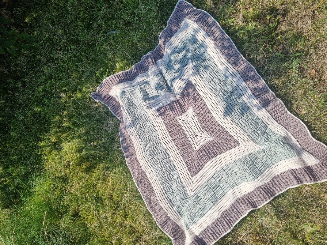 Gehäkelte Babydecke mit Schachbrett- und Sternmuster in Creme, Mint und Mauve auf Gras