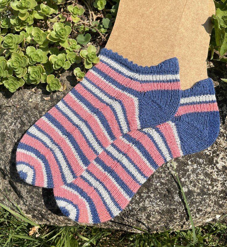 Gestrickte Kurzsocken mit rosa, blauen und weißen Streifen auf einem Sockenblocker