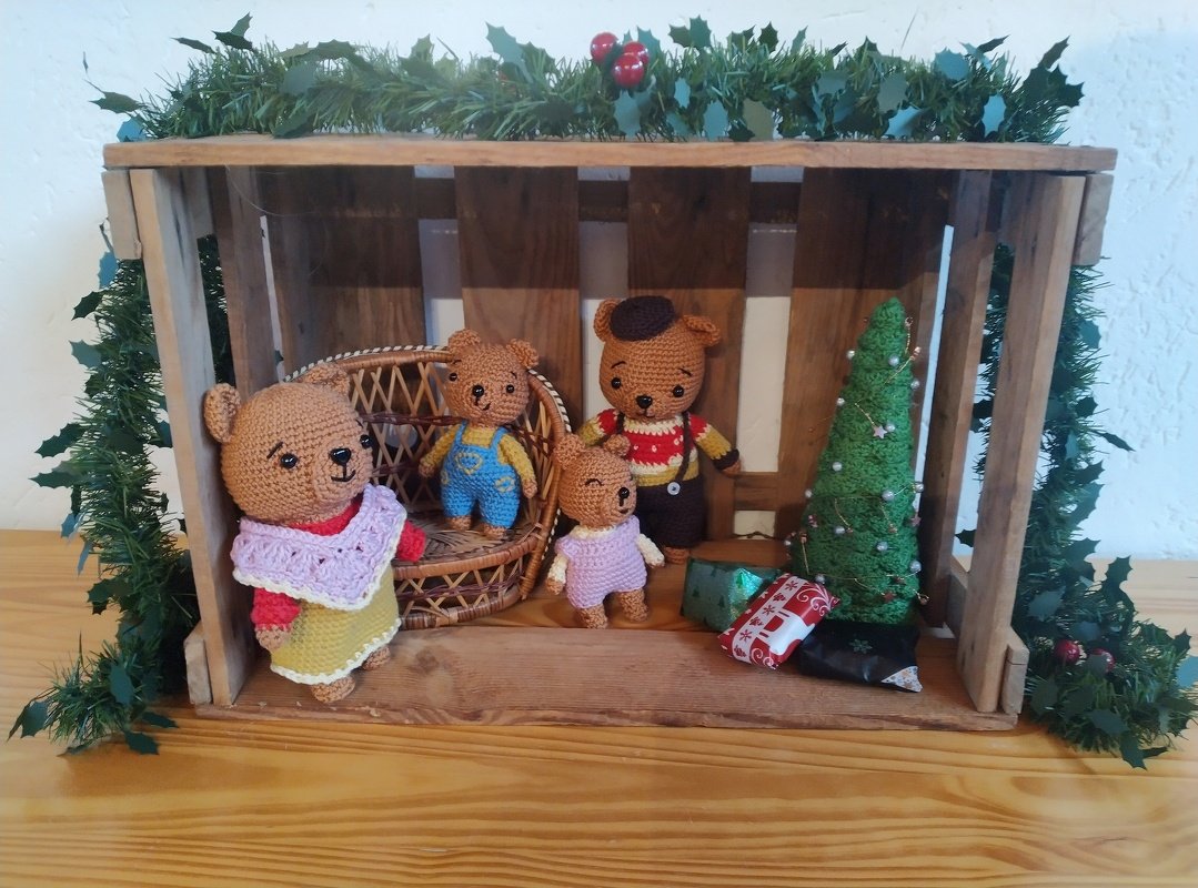Holzkiste mit vier gehäkelten Bärenfiguren, einem kleinen geschmückten Tannenbaum und Geschenkpaketen