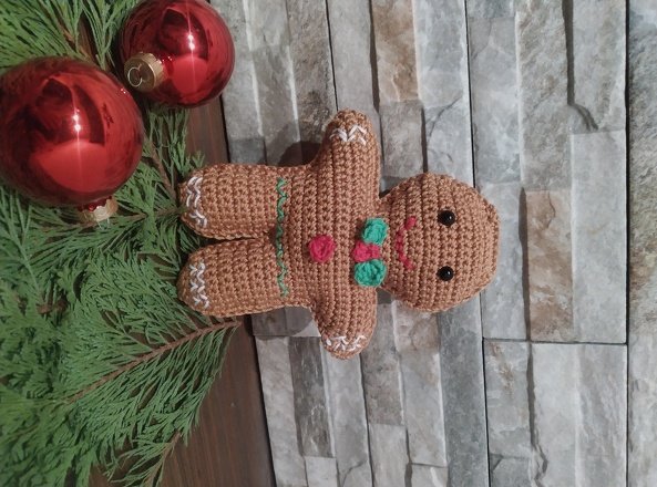 Gehäkelter Lebkuchenmann mit roten Weihnachtskugeln und Tannenzweigen vor Steinwand