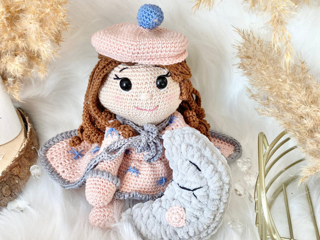Gehäkelte Amigurumi-Puppe in Rosa mit Flügeln hält ein graues Mondkissen