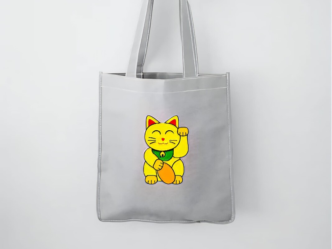 Graue Stofftasche mit gelber Winkekatze in der Mitte
