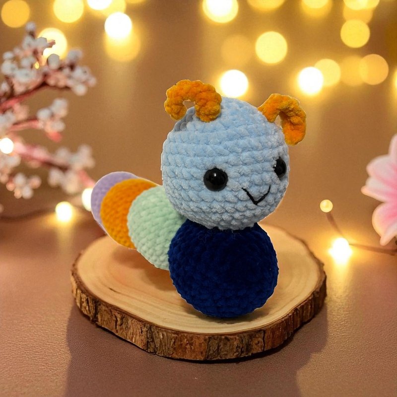 Bunte Amigurumi-Raupe in Blau, Grün, Orange und Lila auf Holzscheibe