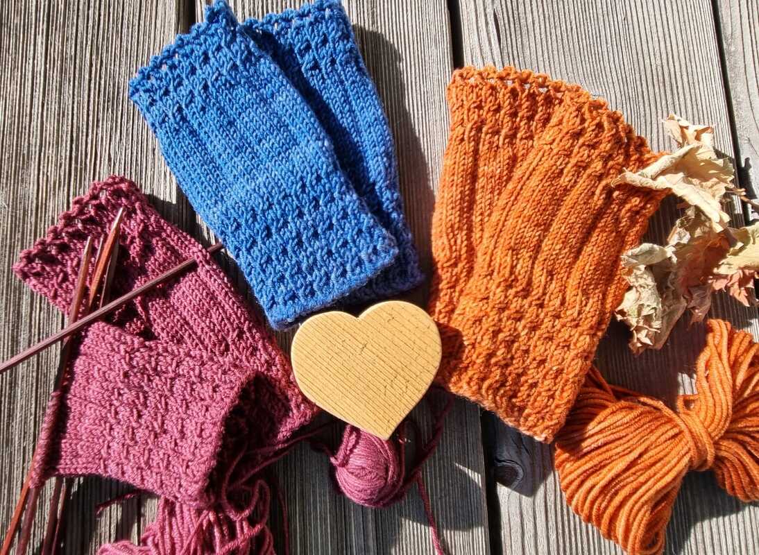Fingerlose Damen-Handstulpen mit Rippenbündchen und strukturiertem Muster neben Stricknadeln und Garn