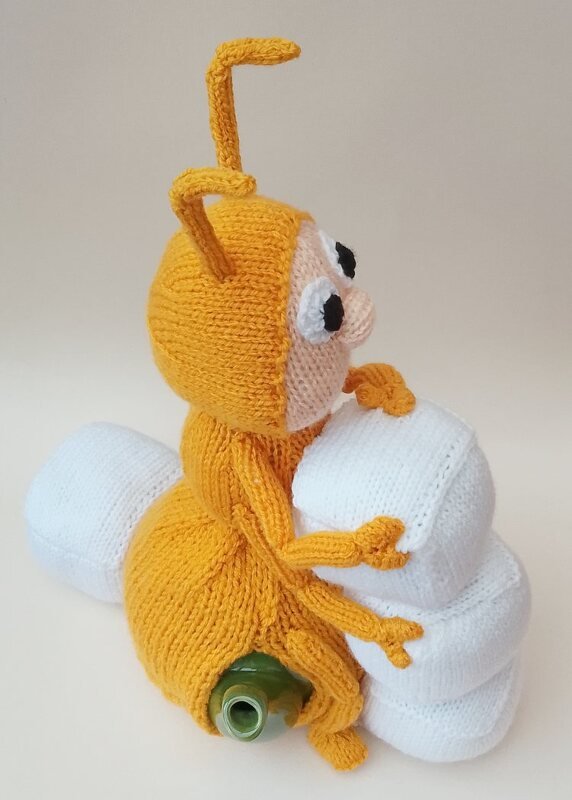 Side view of an orange knitted ant figure with antennae and big eyes holding white knitted blocks