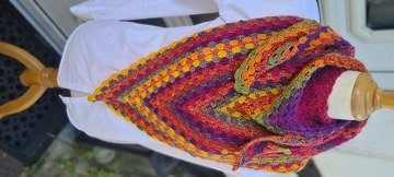 Gehäkeltes Dreieckstuch in Orange-, Gelb-, Pink- und Lilatönen, auf einer weißen Bluse an einer Schneiderpuppe drapiert.