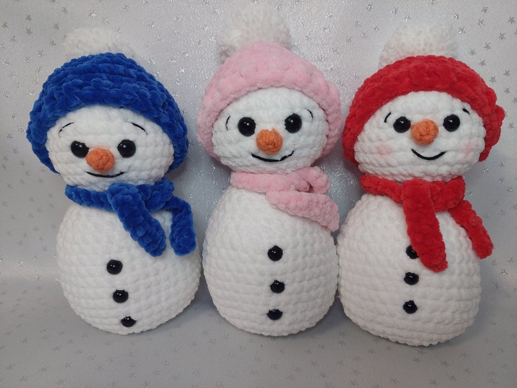 Drei gehäkelte Schneemänner mit blauer, rosa und roter Mütze und Schal