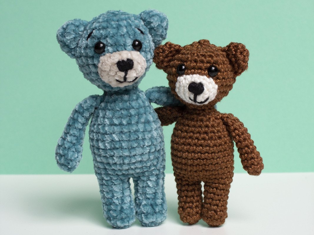 Zwei gehäkelte Amigurumi-Teddys in unterschiedlichen Garntexturen und Farben nebeneinander vor pastellgrünem Hintergrund