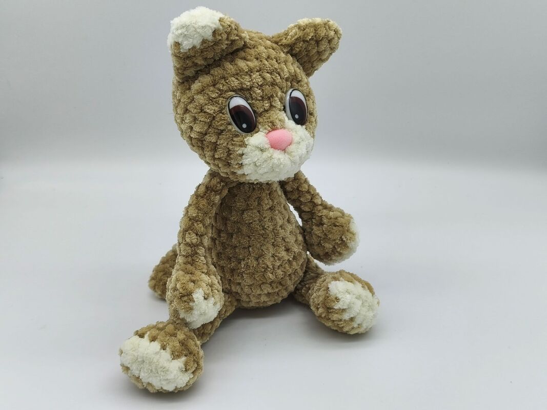 Detailansicht sitzende gehäkelte Amigurumi-Katze in Braun mit weißen Pfoten und rosa Nase