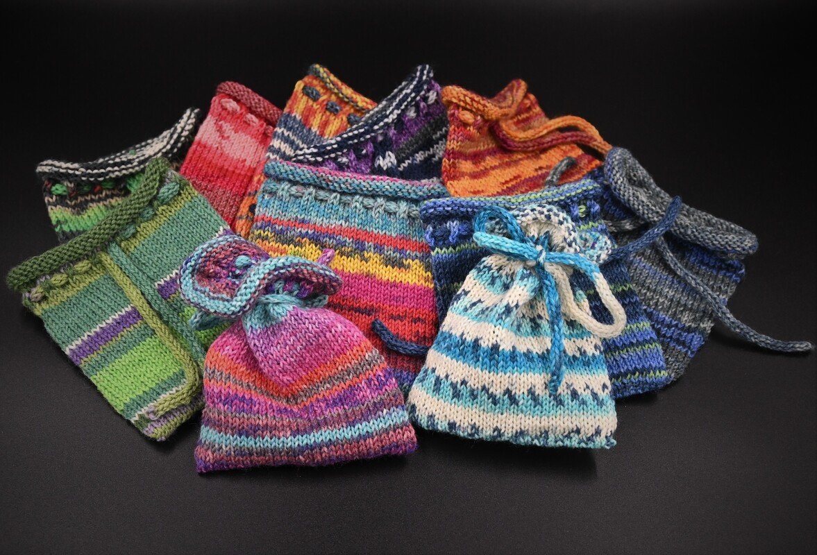 Gestrickte Zugbandsäckchen in bunten Farben und Streifenmustern auf schwarzem Hintergrund.