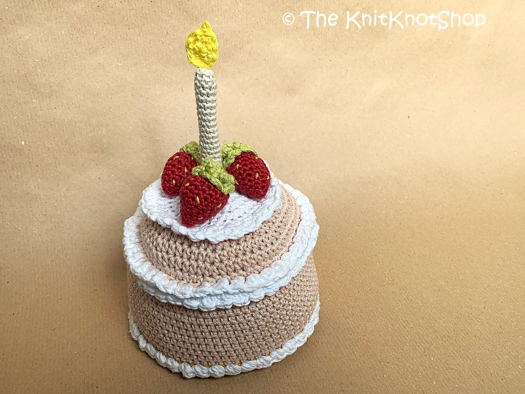 Kompakte gehäkelte Spieltorte mit weißen Borten, Erdbeeren und gehäkelter Kerze