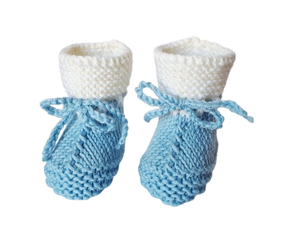 Paar gestrickter Babyschuhe hellblau mit weißem Umschlag und Bändchen