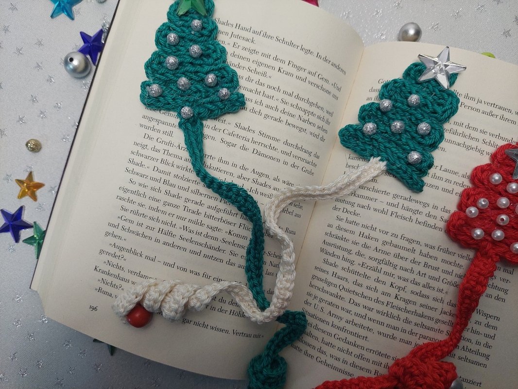 Gehäkelte Tannenbaum-Lesezeichen in Grün und Rot mit Perlen, Sternen und gedrehter Kordel auf offenem Buch