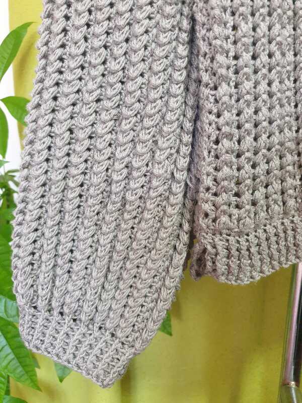 Nahaufnahme von Ärmel und Saum eines gehäkelten grauen Damenpullovers