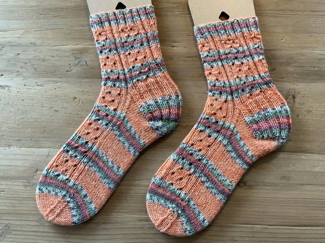 Paar kurzschaftiger handgestrickter Socken in Apricot mit Rippbündchen, Ajourlochmuster und bunten Streifen auf Holzuntergrund