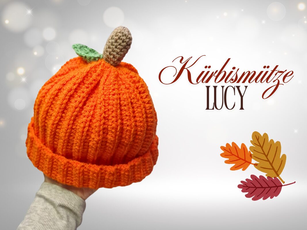 Orange gehäkelte Kürbismütze in Kürbisform mit braunem Stiel und grünem Blatt, in einer Hand gehalten.