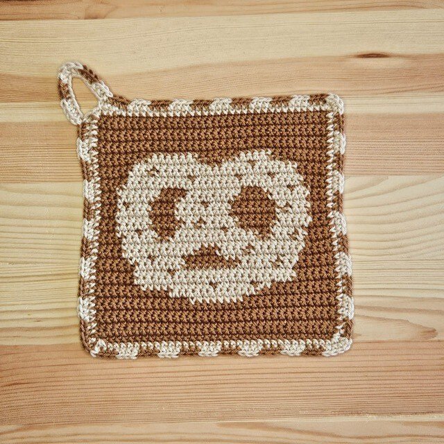 Braun-beiger quadratischer gehäkelter Topflappen mit zentralem Gesichtsmotiv und Aufhängeöse