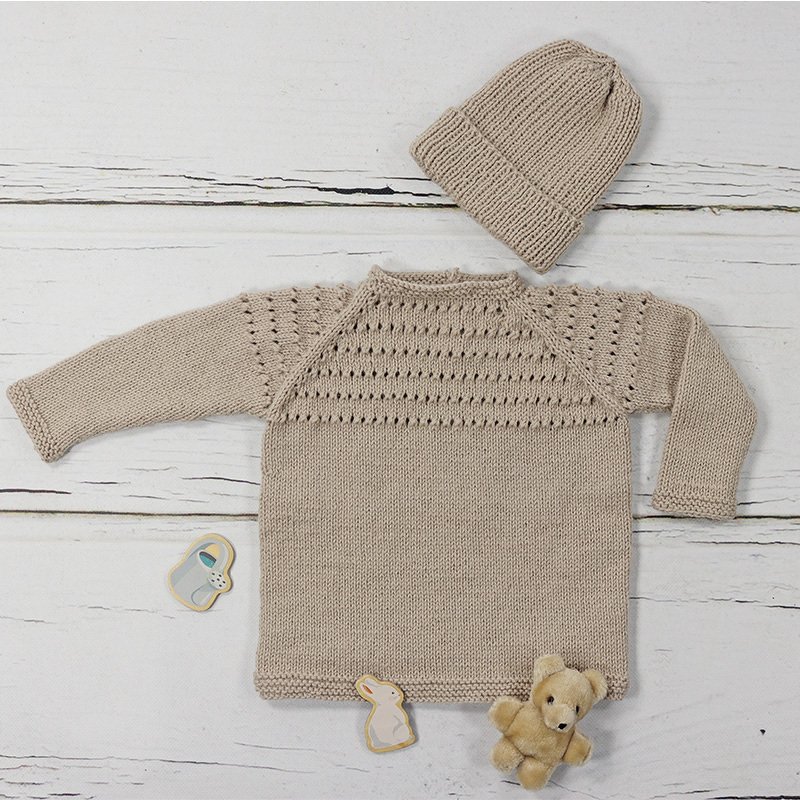Beiger gestrickter Babypullover mit Lochmuster und passender Mütze auf hellem Holzuntergrund