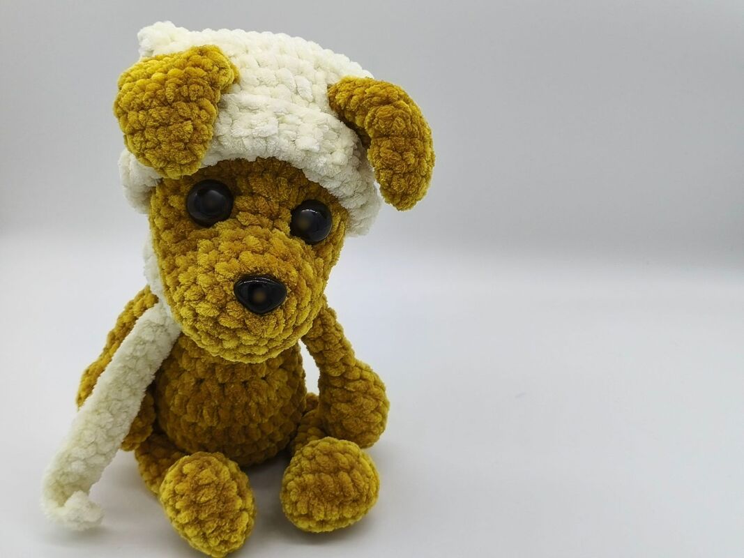 Gehäkelter senfgelber Amigurumi-Hund mit weißer Mütze und Schal