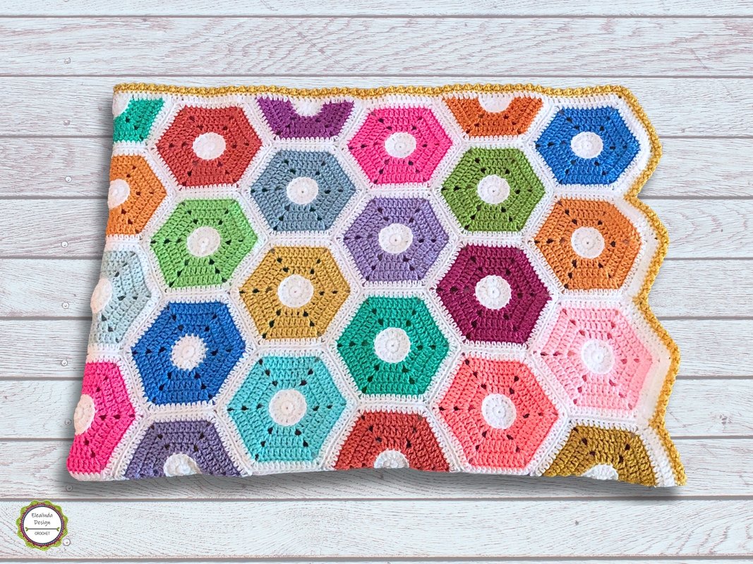 Multicolored hexagon crochet blanket with white joins and yellow scalloped border on light wood background