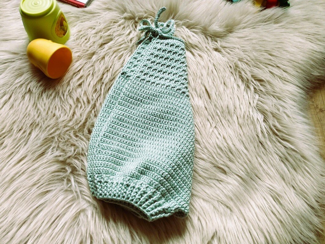 Gehäkelter mintgrüner Säuglingssack mit Kordel auf hellem Fell