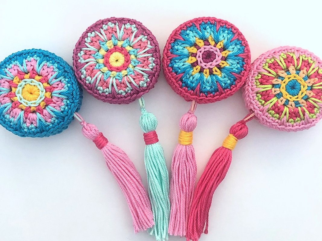Top view of five small round crochet motifs in bright colorways, each finished with a matching yarn tassel.