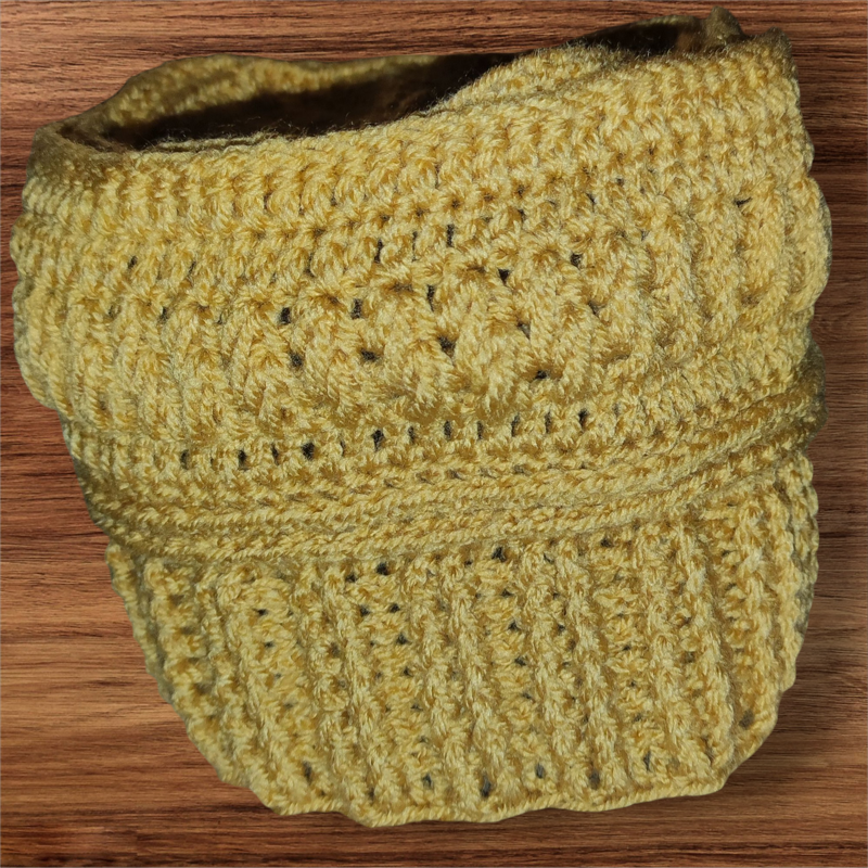 Senfgelbe gehäkelte Mütze mit ausgeprägtem Strukturmuster und geripptem Bund auf Holz