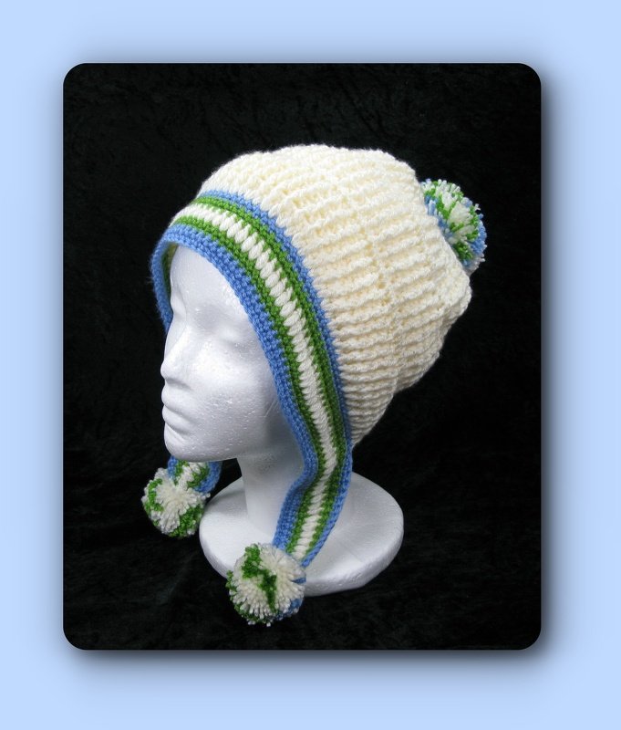 Cremefarbene gehäkelte Mütze mit blau-grünen Streifen an den Ohrenklappen und drei Bommeln auf einer Schaufensterpuppe