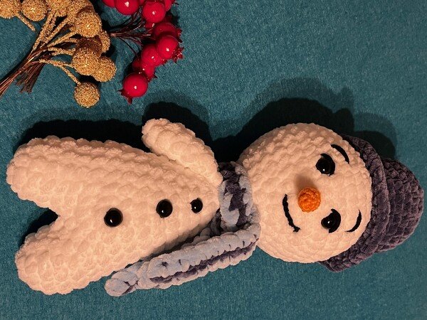 Gehäkelter Amigurumi-Schneemann mit dunkelblauer Mütze und Schal auf türkisfarbenem Hintergrund