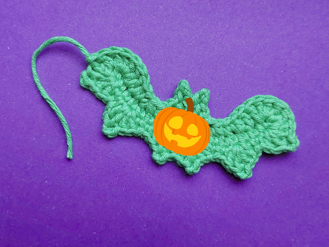Grüne gehäkelte Fledermaus-Applikation mit Faden auf violettem Hintergrund