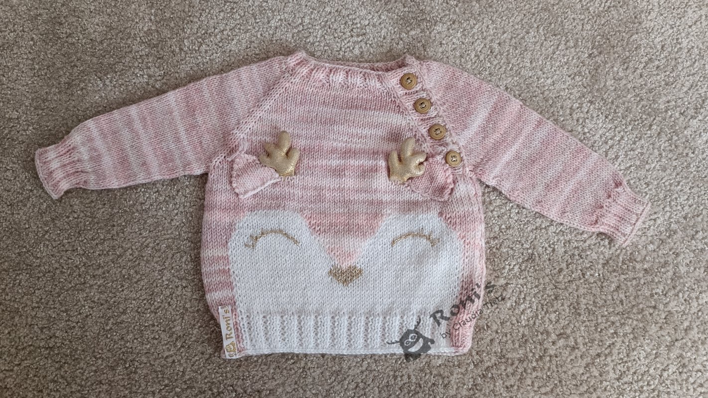 Rosa-weißer gestrickter Baby-Pullover mit Rehgesicht, goldfarbenen Applikationen und Schulterknöpfen, liegend auf Teppich