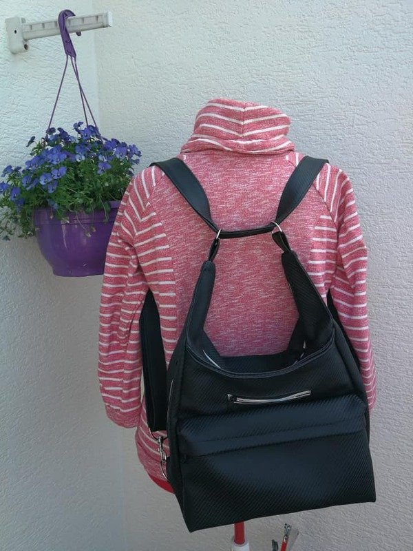 Schwarze wandelbare Tasche mit Reißverschluss, als Rucksack auf einer Schneiderpuppe mit rosa-weiß gestreiftem Oberteil.