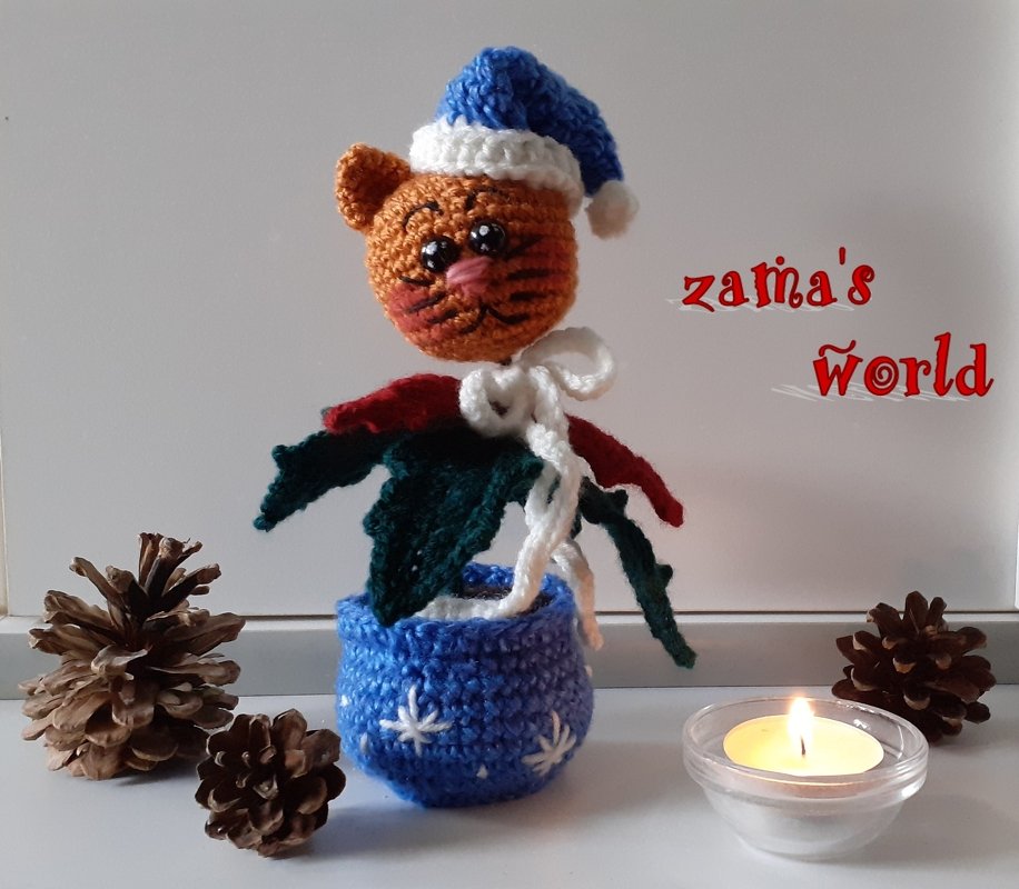 Gehäkelte Amigurumi-Katze mit blauer Mütze in blauem Topf, Kiefernzapfen und brennendem Teelicht