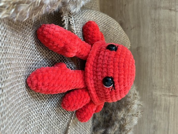 Roter gehäkelter Amigurumi-Oktopus mit großen schwarzen Augen auf rustikalem Stoff