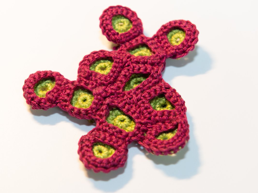 Gehäkeltes Korallen-Element in Magenta mit limettengrünen Innenteilen auf hellem Hintergrund, Nahaufnahme