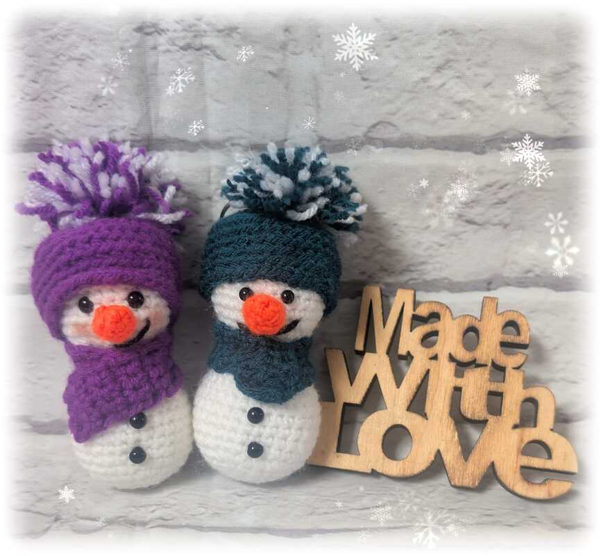 Zwei gehäkelte Amigurumi-Schneemänner mit bunten Mützen und Holzschriftzug