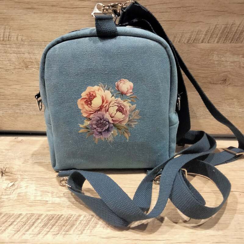 Kleiner blauer Rucksack mit Blumenmotiv vor Holzhintergrund