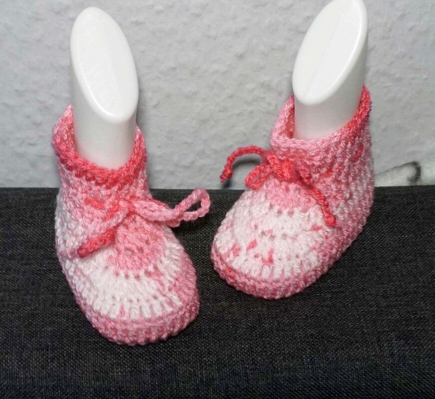 Pink and white crocheted baby booties with laces on white display forms against a gray background.