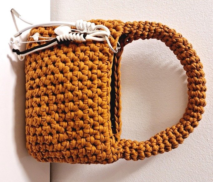 Senfgelbe gehäkelte Henkeltasche mit rundem Griff vor hellem Hintergrund