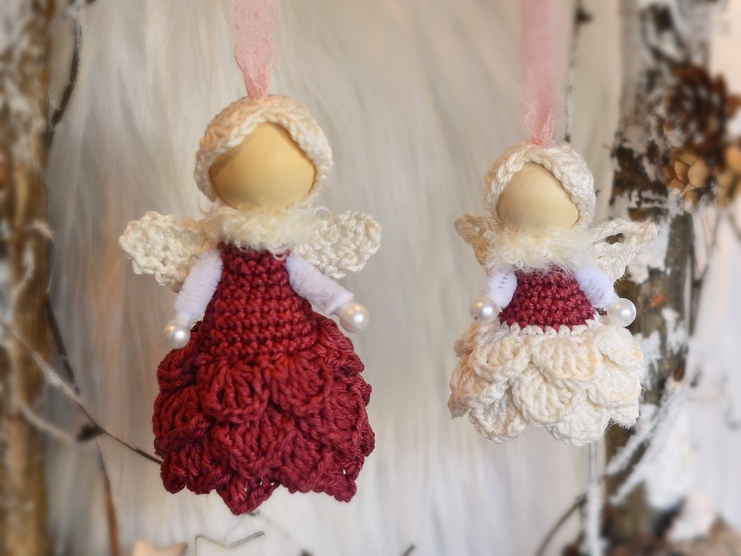 Zwei gehäkelte Amigurumi-Engel in roten und cremefarbenen Kleidern, hängend an Bändern