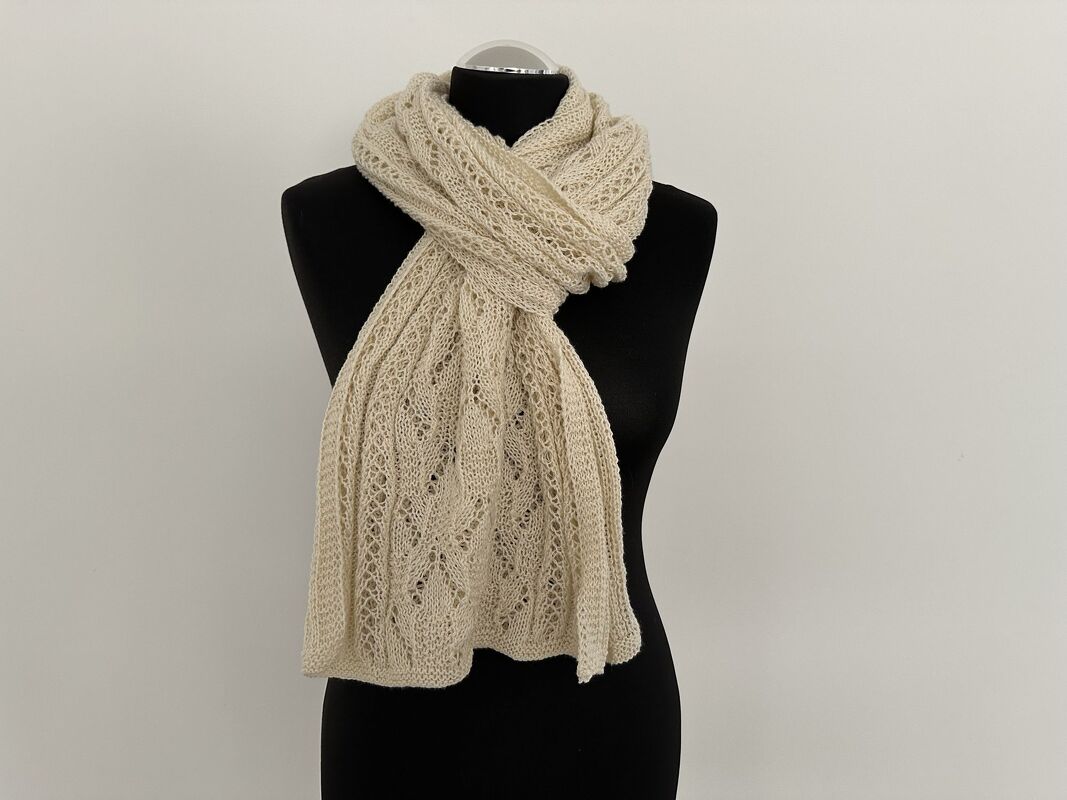 Beiger gestrickter Schal mit Ajour-Lochmuster auf schwarzer Schneiderpuppe.