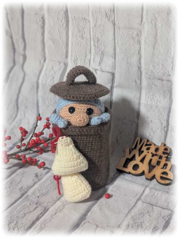 Gehäkelte Amigurumi-Figur mit Hut im braunen Korb, dazu ein weißer gehäkelter Pilz und rote Beeren