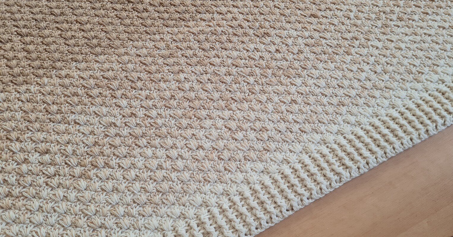 Nahaufnahme einer hellbeigen gehäkelten Decke mit Muschelmuster und gerippter Bordüre.