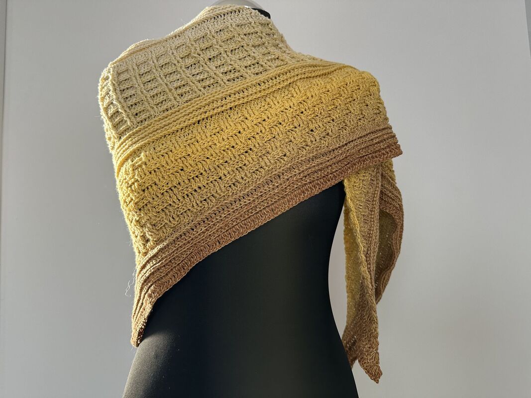Gehäkeltes Dreieckstuch in Gelb‑Braun mit Strukturmuster auf schwarzer Schneiderpuppe