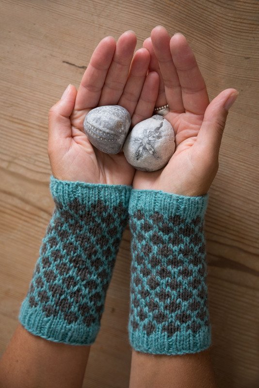 Nahaufnahme von Händen mit fingerlosen Armstulpen in Türkis und Braun, Sicht auf Muster und Bündchen
